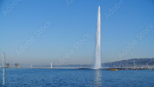 Jet d'Eau (water-jet) in full force on Lake Geneva Switzerland, taken on a clear day, perfect blue wintery skies. Postcard worthy image, capturing Genève's main attraction with small shuttle boat bus