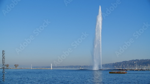 Jet d'Eau (water-jet) in full force on Lake Geneva Switzerland, taken on a clear day, perfect blue wintery skies. Postcard worthy image, capturing Genève's main attraction with small shuttle boat bus
