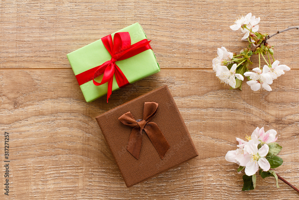 Gift boxes with cherry flowers on the wooden background.