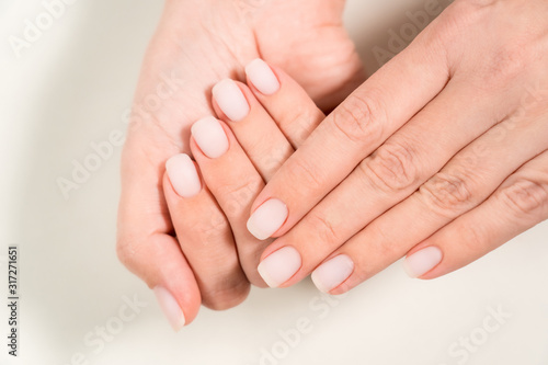 Closeup top view color photography of two beautiful female hands with modern trendy pastel natural manicure naildesign covered with finish mat top without glance. 