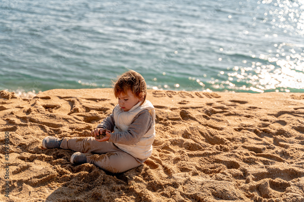 Young child on the sand beach in winter in Spain. Traveling to the nature. Toddler play outdoors