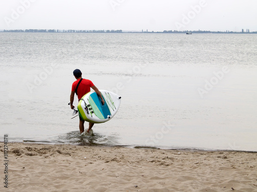 Water sports, surfing. A man with a board in his hands goes to sea. Active holiday, weekend at sea.