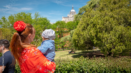 A young caucasian woman chulapa is holding her baby chulapo in traditional dresses with Almudena cathedral during San Isidro, the spring festival in May in the downtown of Madrid, the capital of Spain photo