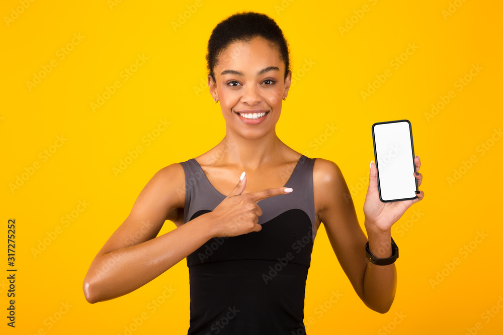 Fit Girl Pointing Finger Showing Smartphone Screen Over Yellow Background Fit Girl Pointing Finger Showing Smartphone Screen Over Yellow Background
