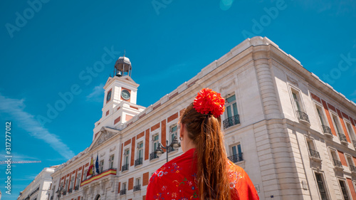 A young caucasian woman chulapa with red flower, traditional dress, and Spanish scarf at Puerta del Sol during San Isidro, the spring festival in May in the downtown of Madrid, the capital of Spain photo