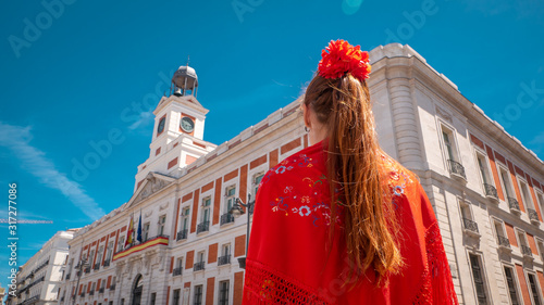 A young caucasian woman chulapa with red flower, traditional dress, and Spanish scarf at Puerta del Sol during San Isidro, the spring festival in May in the downtown of Madrid, the capital of Spain photo