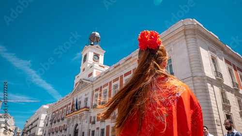 A young caucasian woman chulapa with red flower, traditional dress, and Spanish scarf at Puerta del Sol during San Isidro, the spring festival in May in the downtown of Madrid, the capital of Spain photo