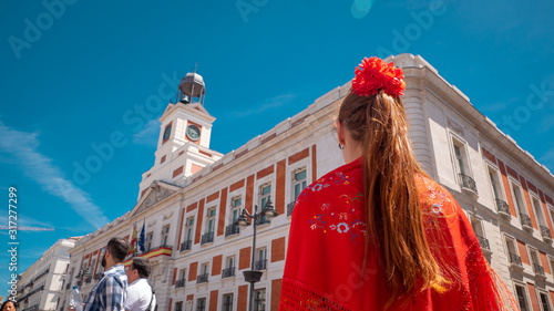 A young caucasian woman chulapa with red flower, traditional dress, and Spanish scarf at Puerta del Sol during San Isidro, the spring festival in May in the downtown of Madrid, the capital of Spain photo