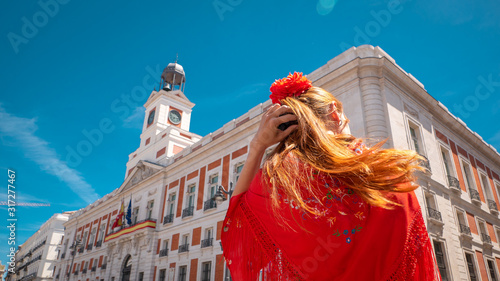 A young caucasian woman chulapa with red flower, traditional dress, and Spanish scarf at Puerta del Sol during San Isidro, the spring festival in May in the downtown of Madrid, the capital of Spain photo