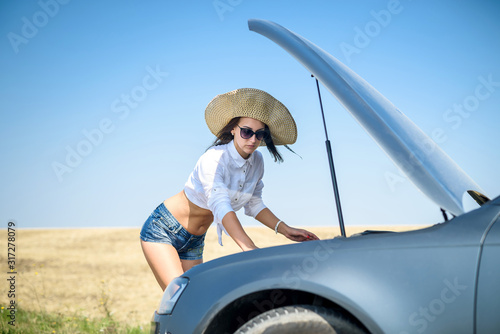 Pretty  young woman looking at the engine of broken car. Road trip problems © RomanR