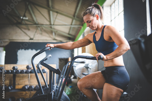 Female fitness model exercising on an elliptical training bike in a gym © Dewald