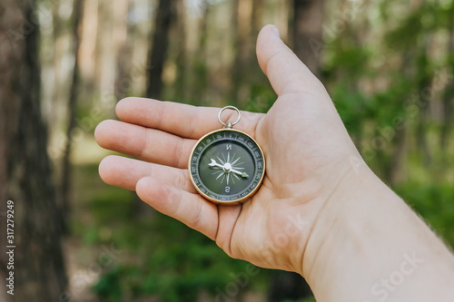 Compass in a guy s hand on the background of the forest. Concept on the theme of tourism.