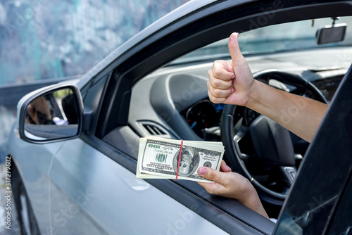 Bribe concept. Female hands giving dollar bundle inside car close up