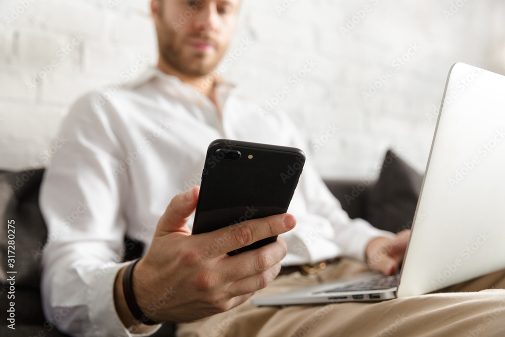 Photo of businessman holding cellphone and using laptop in apartment Photo of businessman holding cellphone and using laptop in apartment