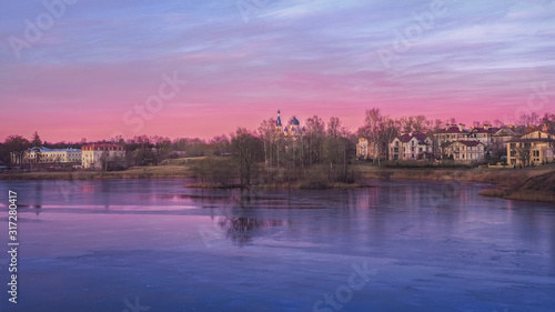 Panorama of a purple sunset with a rural landscape with houses on the lake.