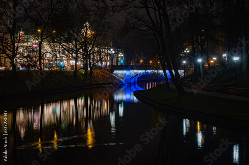 Riga's City Canal by night with the city lights reflecting in the water in foggy evening and small bridge lightened with blue light during Staro Riga festival