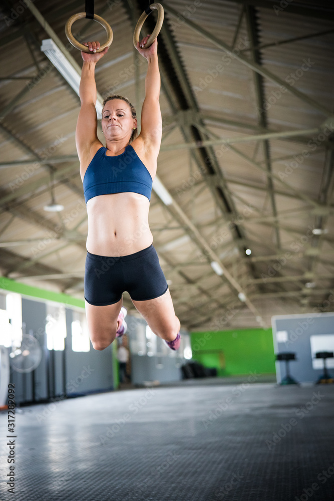 Female fitness model doing cross fit training on over head rings in a gym by pulling herself up Female fitness model doing cross fit training on over head rings in a gym by pulling herself up