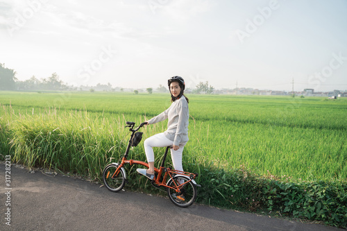 young women wear helmets to ride folding bikes for sports in rice fields background