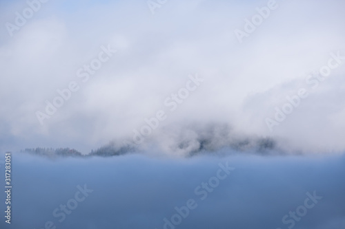 Fluffy clouds in evening overcast sky view. Mountain tops silhouettes in mist and clouds.