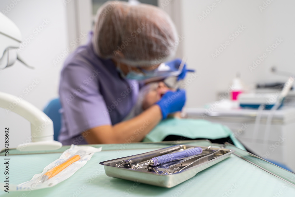 Naklejka premium in the foreground is the focus of dental instruments, in the background is out of focus the dentist is treating the patient.