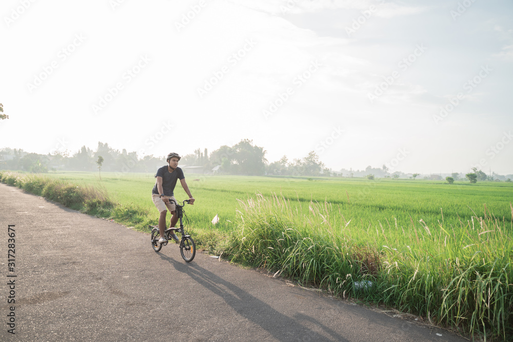 young male wear helmets to ride folding bikes for sports in rice fields background