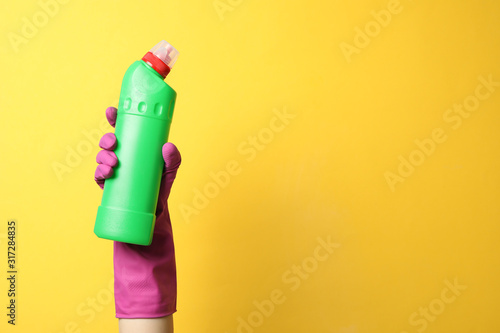 Hand in cleaning glove hold bottle with detergent on yellow background, space for text