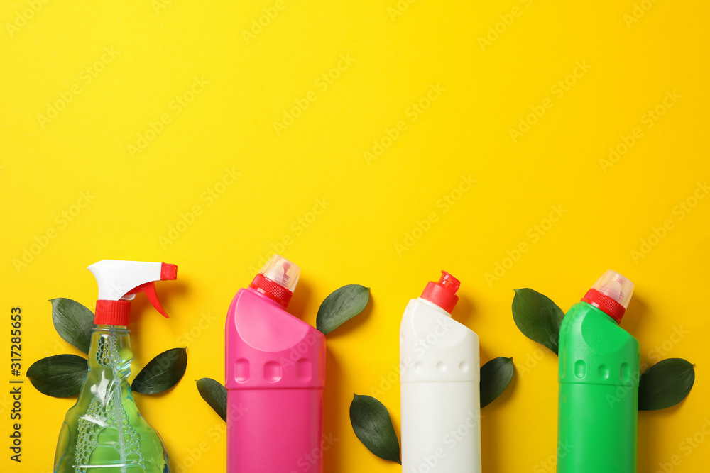 Bottles with detergent and leaves on yellow background, space for text
