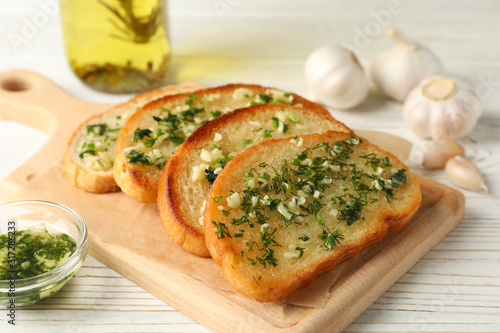 Board with garlic bread on white wooden background, close up