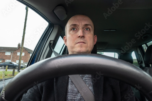 A middle aged man sat in the driving seat of a car.