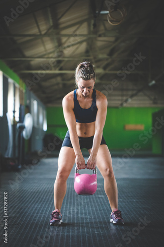 Female fitness model doing kettle bell exercises in a cross fit gym