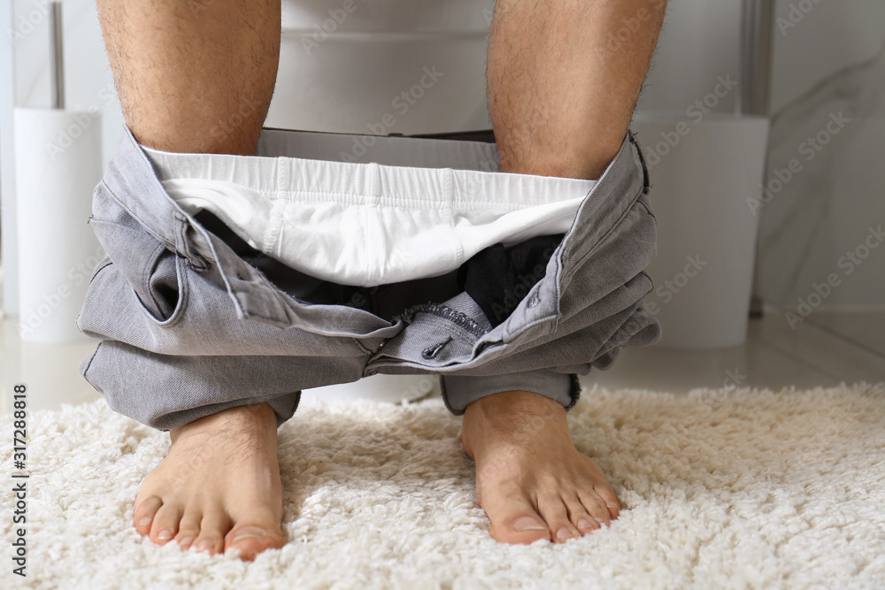 Man sitting on toilet bowl in bathroom, closeup Man sitting on toilet bowl in bathroom, closeup