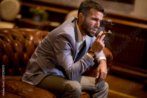 Handsome man sitting on a leather sofa and smoking cigar