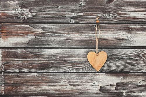 A wooden heart hangs on an old dark shabby wall from wooden boards. Greeting card. Copy space.