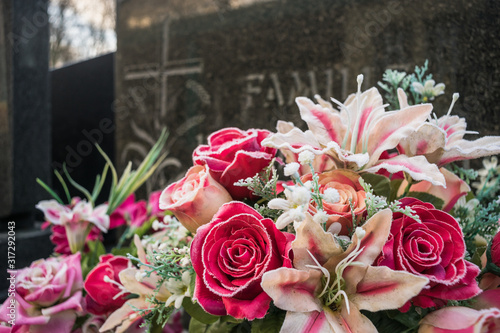 Fototapeta Naklejka Na Ścianę i Meble -  Family grave with artificial flowers and roses in the foreground and white frost