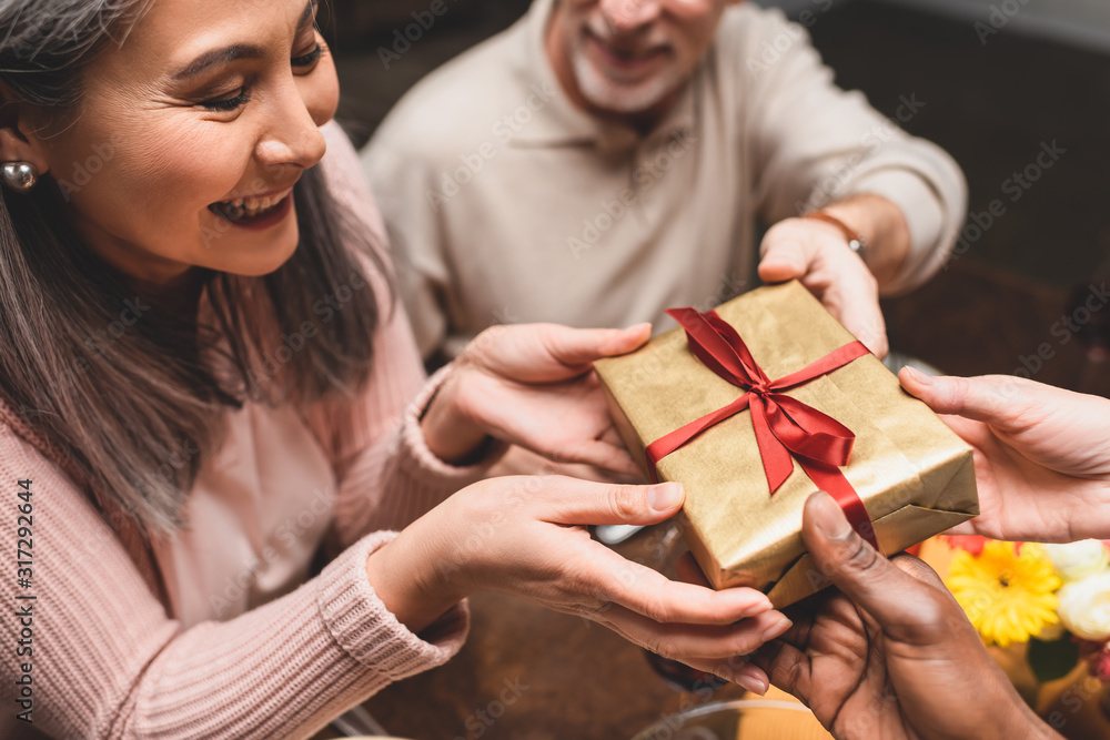 cropped view of multicultural friends giving present to smiling asian woman during dinner cropped view of multicultural friends giving present to smiling asian woman during dinner