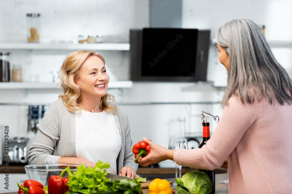 smiling woman cooking and talking with her friend with bell pepper