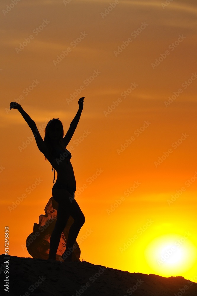 Silhouette of woman in bikini standing and holding pareo in raised hands