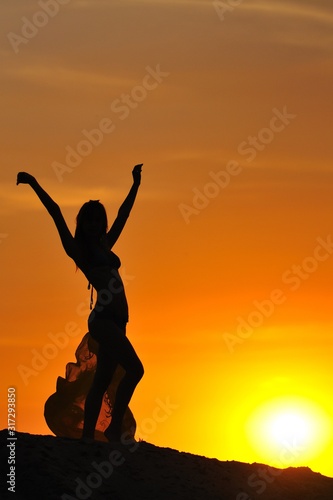 Silhouette of woman in bikini standing and holding pareo in raised hands