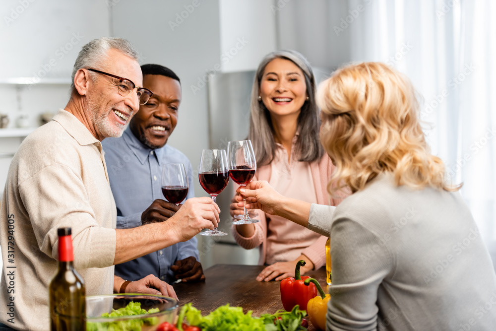 smiling multicultural friends clinking with wine glasses in kitchen smiling multicultural friends clinking with wine glasses in kitchen