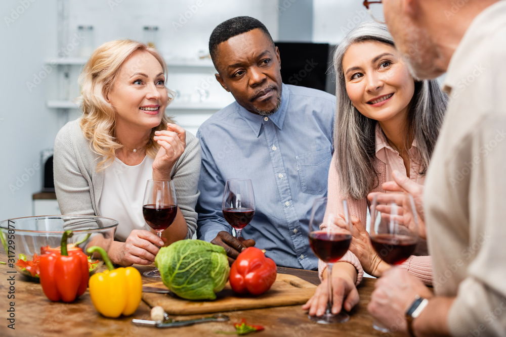 selective focus of multicultural friends talking and holding wine glasses