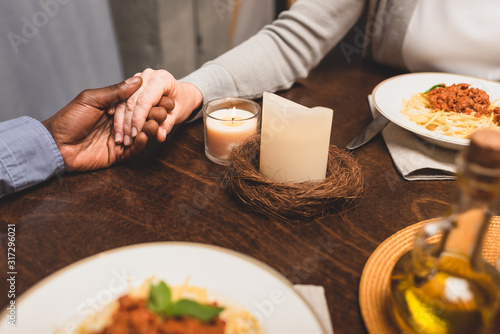 cropped view of african american man holding hand of friend and praying during dinner