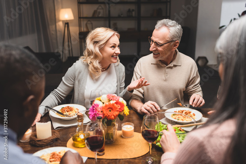 selective focus of smiling man and woman talking with multicultural friends during dinner