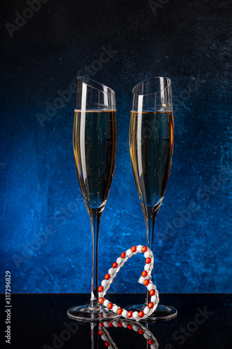 Two glasses with champagne on a black mirror surface. Heart for St. Valentine. Blue background Concrete wall. Black glass. Crystal glass