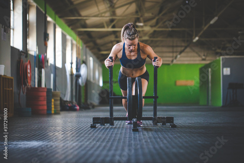 Fotografi Female fitness model pushing a sled in a cross fit gym.