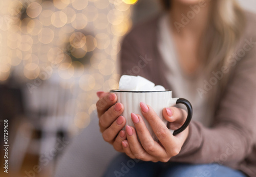 Woman warming hands with cup of cocoa with marshmallows