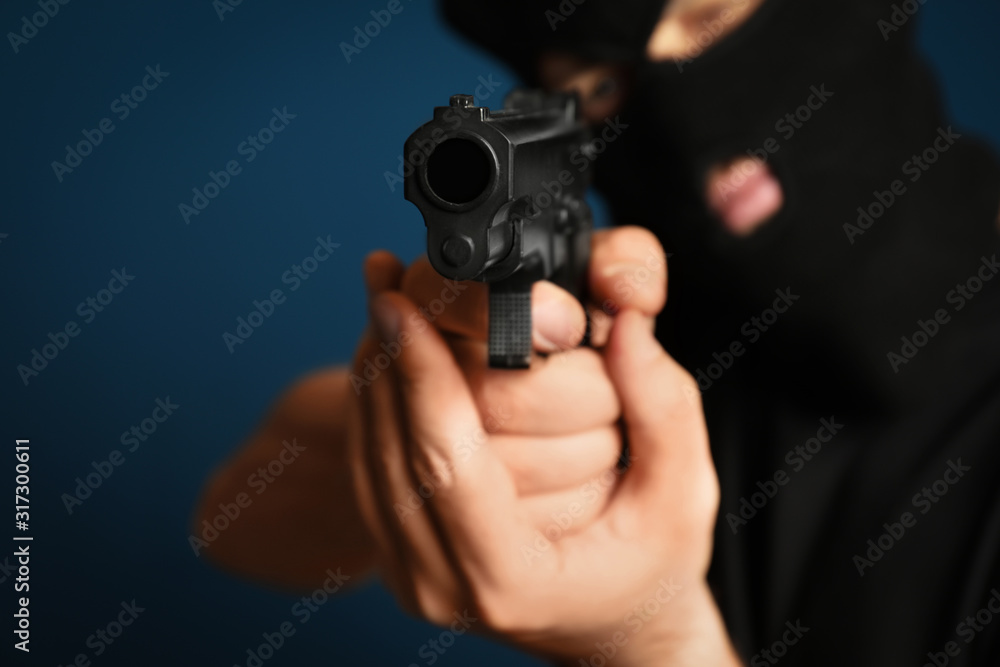 Man in mask holding gun against dark blue background, focus on hands Man in mask holding gun against dark blue background, focus on hands