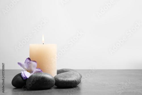Spa stones, burning candle and freesia flower on grey table, space for text