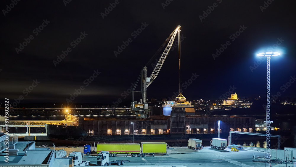 mechanical hydraulic clamshell grabbers loading coal on ship at night.