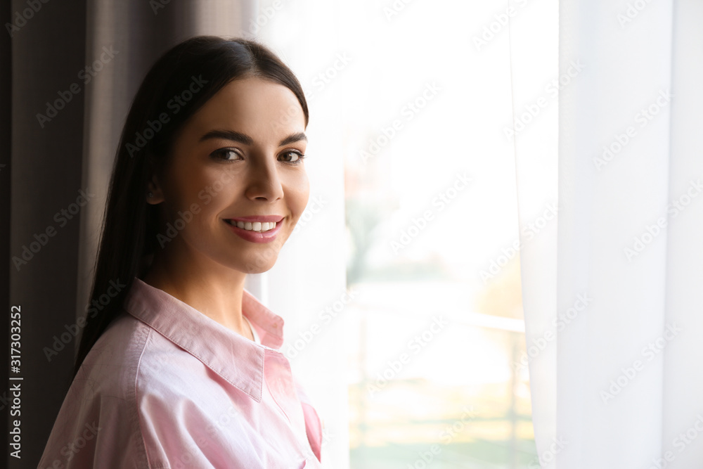 Woman near window with beautiful curtains at home. Space for text