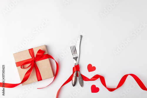 Romantic setting on white background. Valentines day card template. Kraft gift box with red ribbon, paper hearts, silverware. Concept anniversary, mother birthday, place for text, copyspace, top view